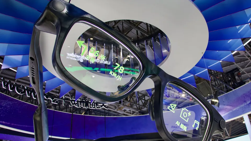 An oversized pair of black Alibaba Quark smart glasses hanging at a trade show, with green navigation arrows, speed readings and camera icons shown on the lenses