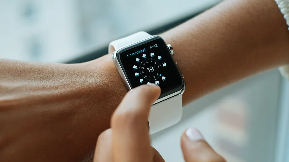 A person taps the screen of an Apple Watch with a white band showing a weather watch face
