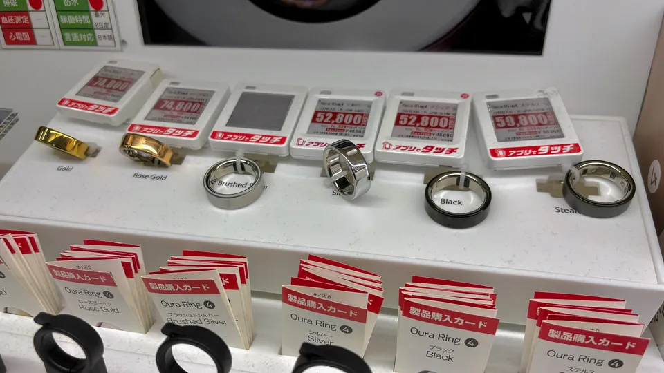 Oura rings in gold, rose gold, brushed silver, silver, black and stealth finishes on a store display, with electronic price tags and purchase cards