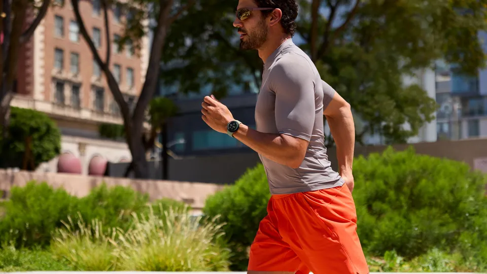 A man running outdoors in a gray T-shirt and orange shorts, wearing a Google Pixel Watch 5.
