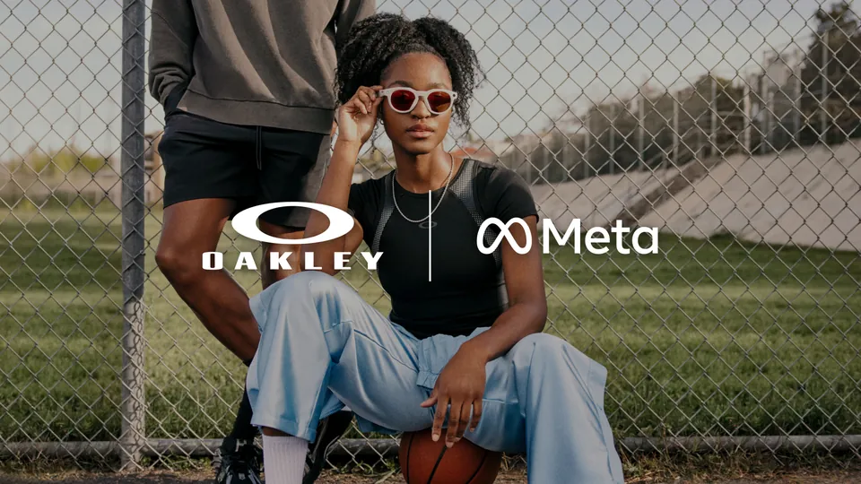 A young woman in a black T-shirt and light blue pants sits in front of a chain-link fence, holding white-framed glasses on her face, with the Oakley and Meta logos across the middle of the image