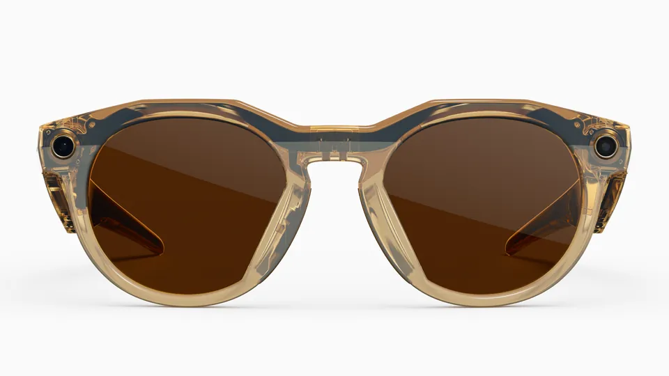Front view of translucent light-brown round Oakley Meta HSTN glasses with brown lenses and a camera on each side, on a white background
