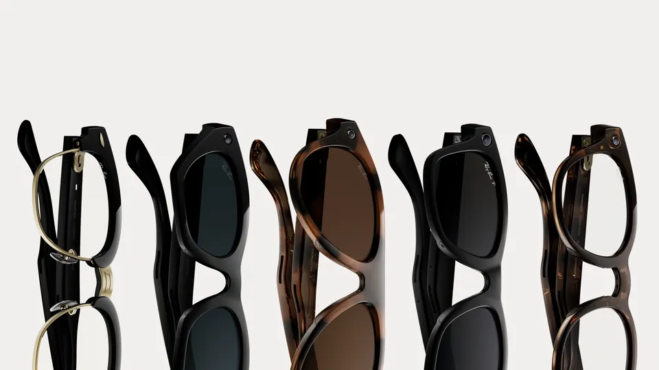 Five pairs of Ray-Ban Meta glasses standing on their sides in a row, in black, tortoiseshell and gold-trimmed styles, on a pale background