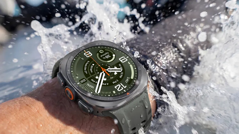 A wrist wearing a Galaxy Watch Ultra2 with a green band and a green analog watch face, water splashing around it