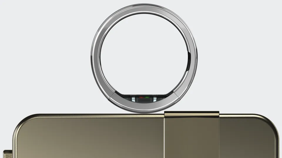 A polished silver smart ring with a small sensor window on its inner band balanced on the edge of a bronze-colored charging case, against a light gray background