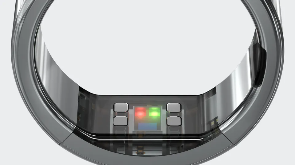 Close-up of the inside of a titanium smart ring showing its sensor window with red and green lights and four small contact pads, against a light gray background