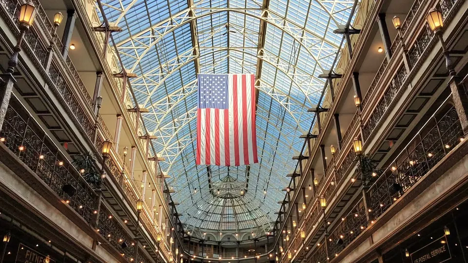 The interior of The Arcade in Cleveland, with an American flag hanging beneath a glass roof and tiers of balconies lit by warm lamps on both sides