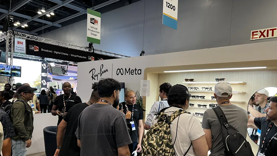 The Ray-Ban and Meta booth at a trade show, with rows of Ray-Ban Meta frames on lit wooden shelves and visitors gathered in front of it