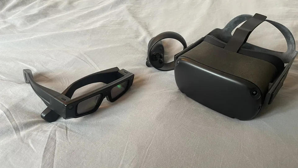 Black fifth-generation Snap Spectacles AR glasses lying on a white sheet next to a Meta Quest VR headset and controller