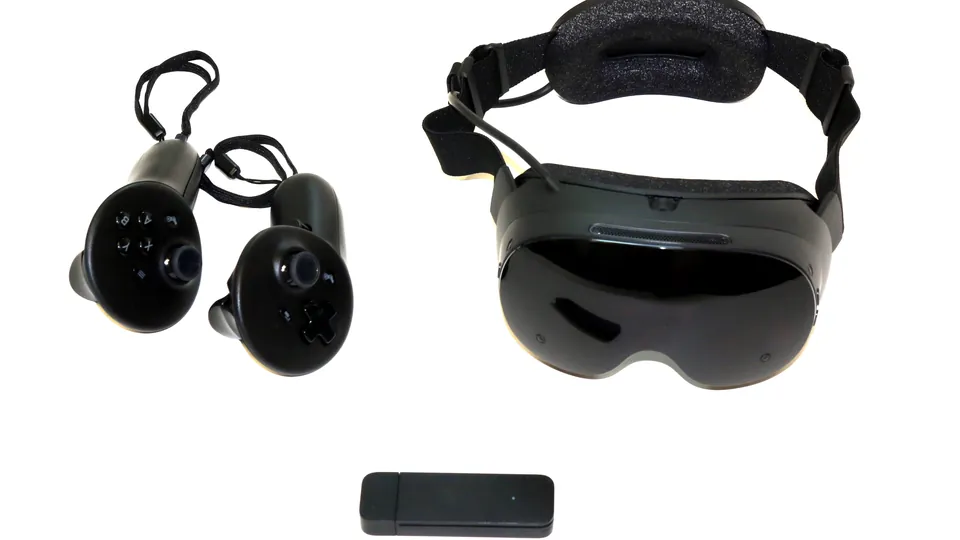 A black Steam Frame headset with a fabric strap beside two black controllers and a small black wireless adapter on a white surface