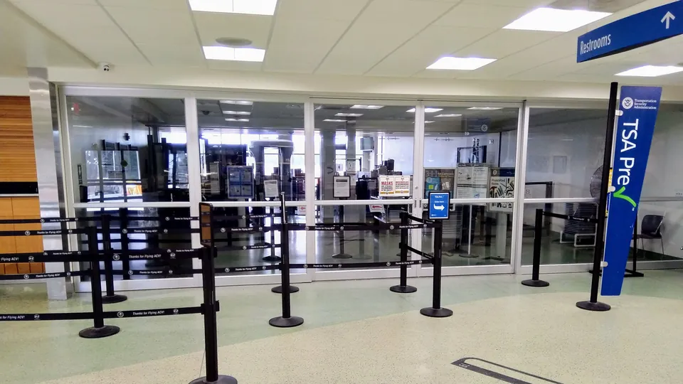 An empty airport security queue marked off with black stanchions in front of a glass-walled TSA checkpoint, with a blue TSA PreCheck sign on the right